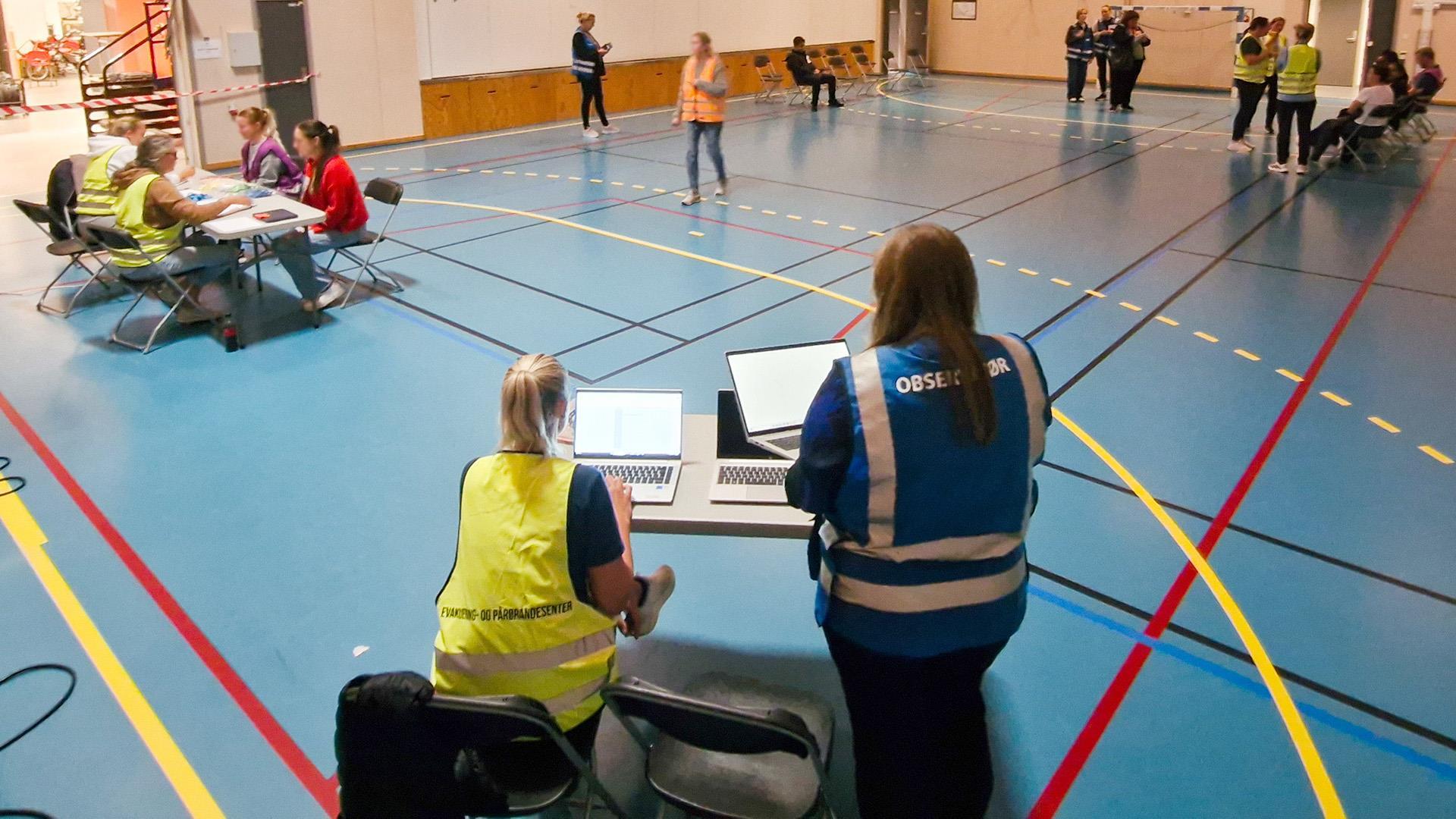 Personar ein gymsal, nokre i gule og blå vestar