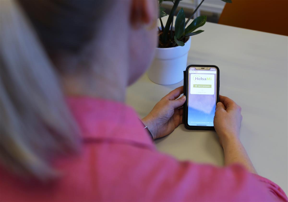 Kvinne holder mobil med HelsaMi app - Klikk for stort bilete