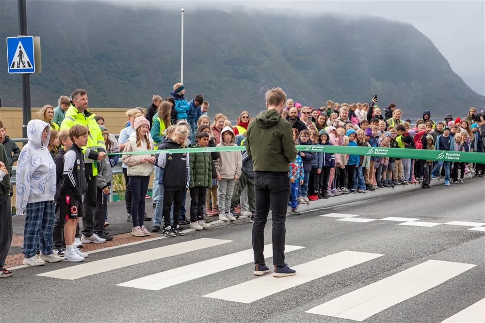 Mann klipper et bånd med Bypakke Ålesund-logo foran en forsamling - Klikk for stort bilete