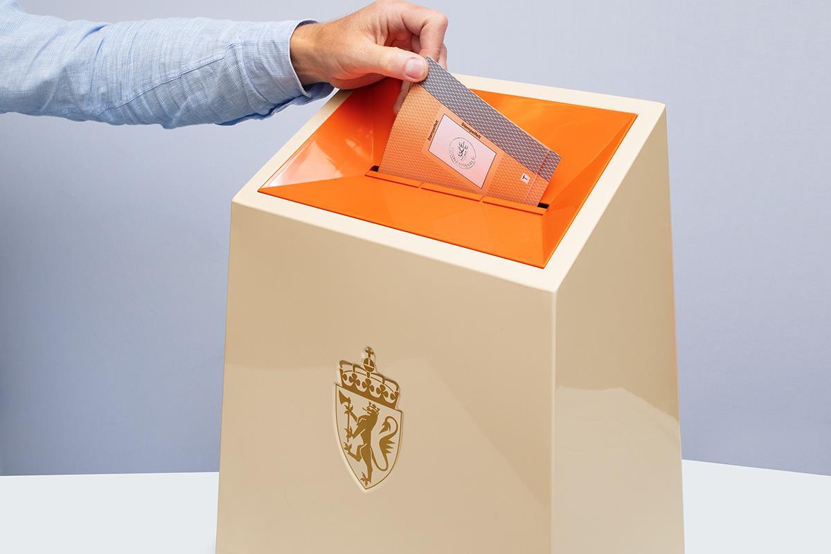 Ei hånd som held ein stemmeseddel i luka på ei valgurne